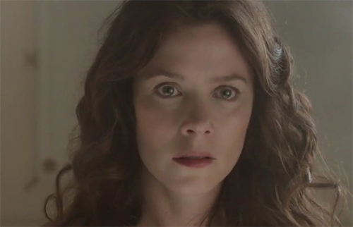 Close-up of a woman with long wavy brown hair, looking directly at the camera with wide eyes and a slightly open mouth